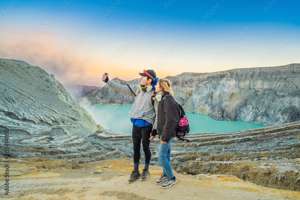 Young tourist man and woman stand at the edge of the crater of the Ijen volcano or Kawah Ijen on the Indonesian language. Famous volcano containing the biggest in the world acid lake and sulfur mining