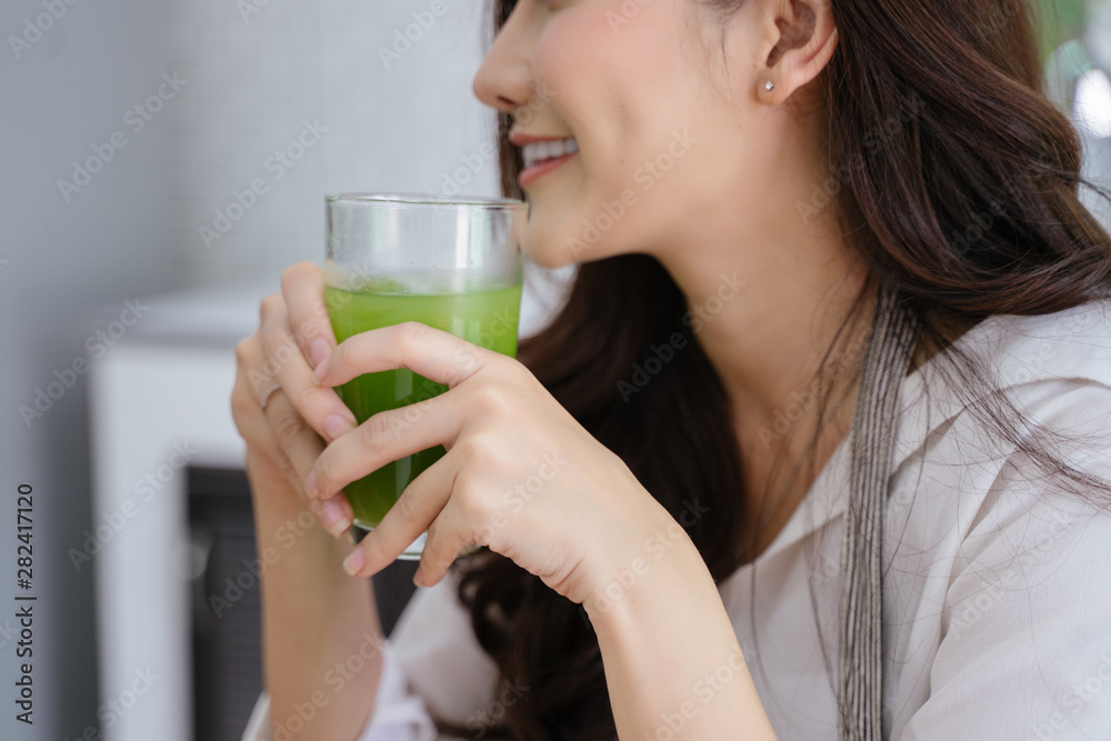 young girl drinking green cocktail with a straw.Woman drinking a homemade green detox juice. texting on her phone while sitting in her kitchen table young girl drinking green cocktail with a straw.Woman drinking a homemade green detox juice. texting on her phone while sitting in her kitchen table