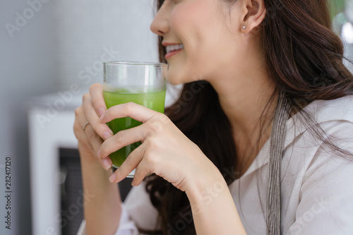 young girl drinking green cocktail with a straw.Woman drinking a homemade green detox juice. texting on her phone while sitting in her kitchen table 