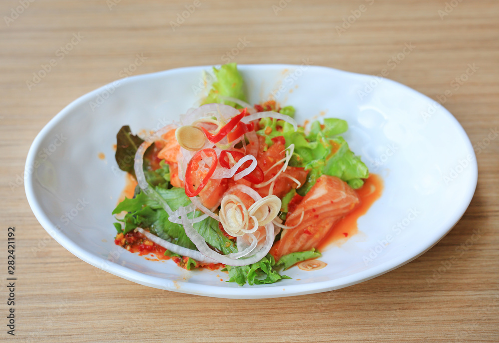 Spicy salmon salad in white plate on wooden table. Japanese food. Spicy salmon salad in white plate on wooden table. Japanese food.