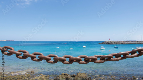 Seascape of blue water behind a heavy metal chain link barrier.