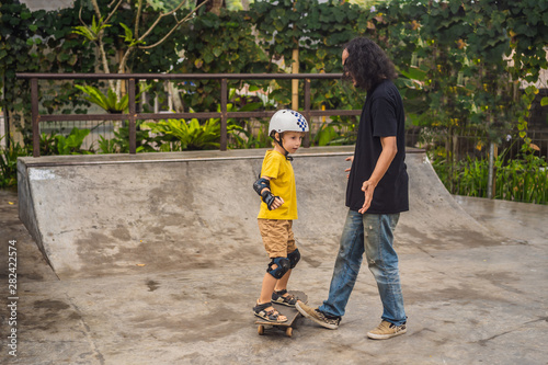 Athletic boy learns to skateboard with a trainer in a skate park. Children education, sports