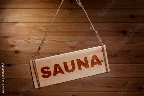 Wooden signboard with the words SAUNA on a rough rope on a beautiful wooden background