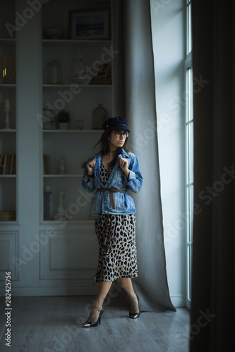 Fashion portrait of young beautiful female model standing in leopard dress in interior studio.