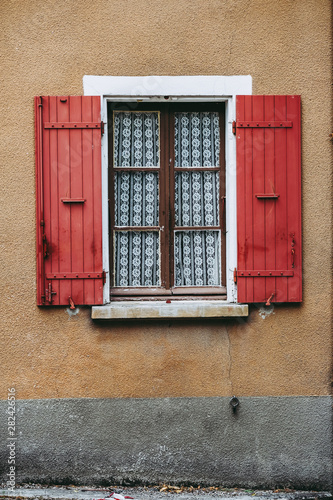 Fenêtre avec des rideaux de dentelle et volets en bois rouge