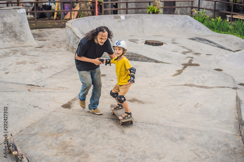 Athletic boy learns to skateboard with a trainer in a skate park. Children education, sports