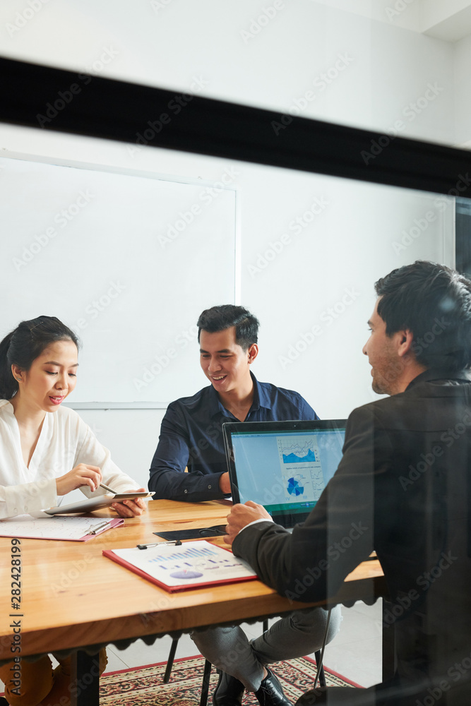 Young businesswoman sitting at the table using digital tablet and talking to her partners while they listening to her during a meeting