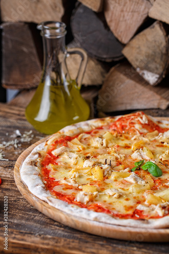 Pizza with chicken and pineapple on the background of firewood and olive oil photo