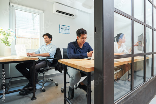 Young business people sitting at workplaces busy with their work and using computers at modern office