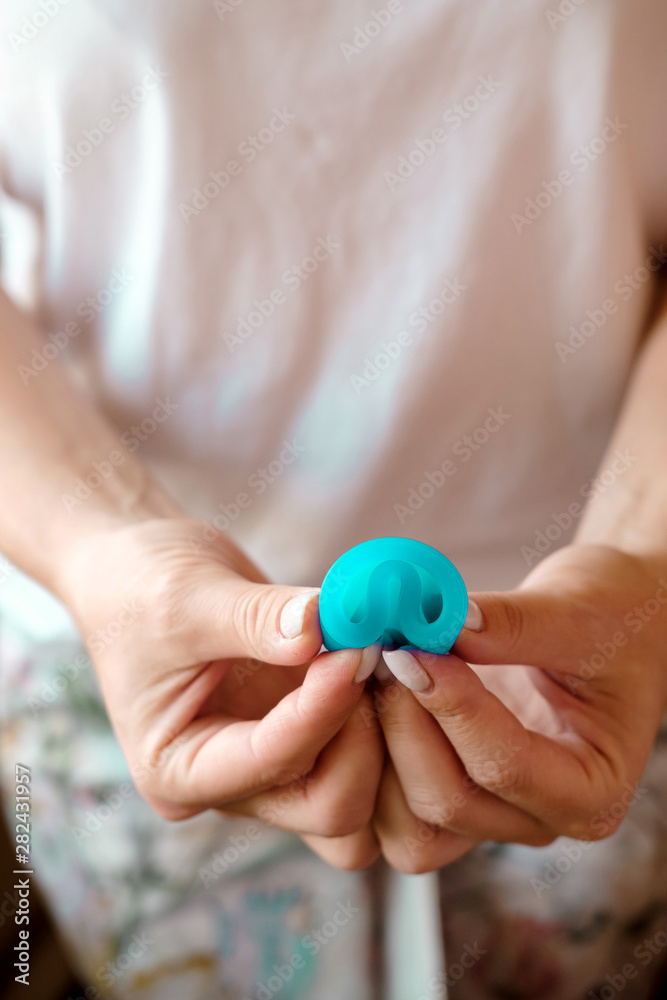 Woman holding in hands folded blue menstrual cup. Feminine hygiene alternative product instead of tampon during period. Menstruation, critical days, women periods. Zero waste, eco, ecology. Close up Woman holding in hands folded blue menstrual cup. Feminine hygiene alternative product instead of tampon during period. Menstruation, critical days, women periods. Zero waste, eco, ecology. Close up