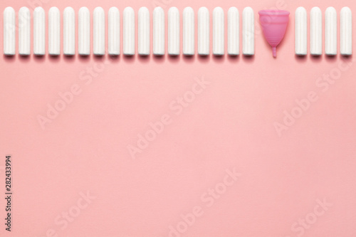 Reusable silicone menstrual cup and heap of tampons comparison on a soft pink background. Modern female intimate alternative gynecological hygiene. Eco zero waste concept. Copy space place for text