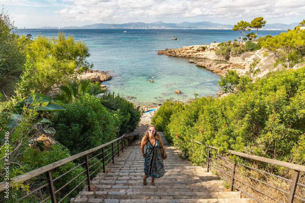 Woman vacationers taking picture on paradisiaca island with turquoise sea in Balearic Islands. Vacation Girl Landing Glasses on Beach Stairs