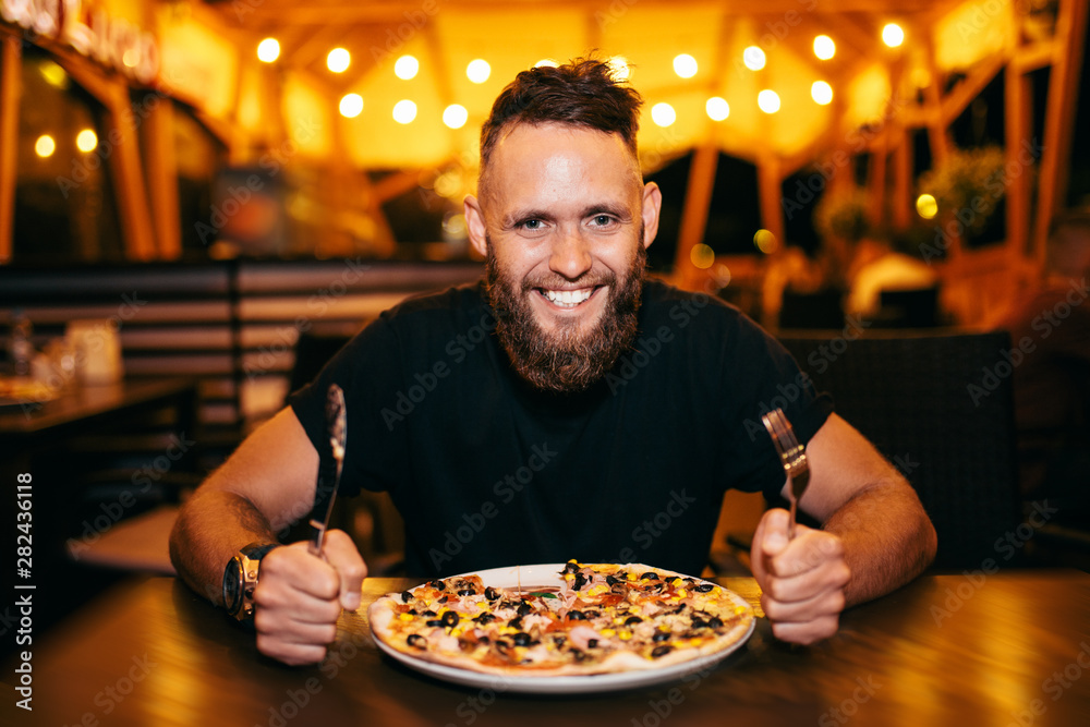 Happy hungry man eating pizza in a bar.