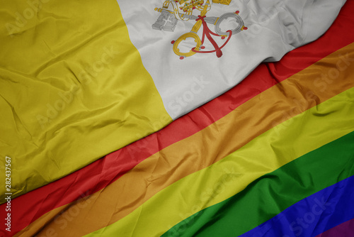 waving colorful gay rainbow flag and national flag of vatican city.
