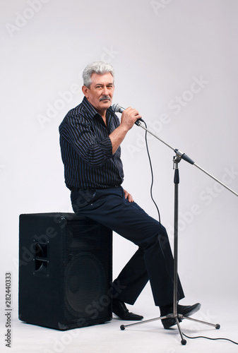 singer, musical performer, gray-haired man singing into a microphone, sitting on a musical column in the studio. on a white background
