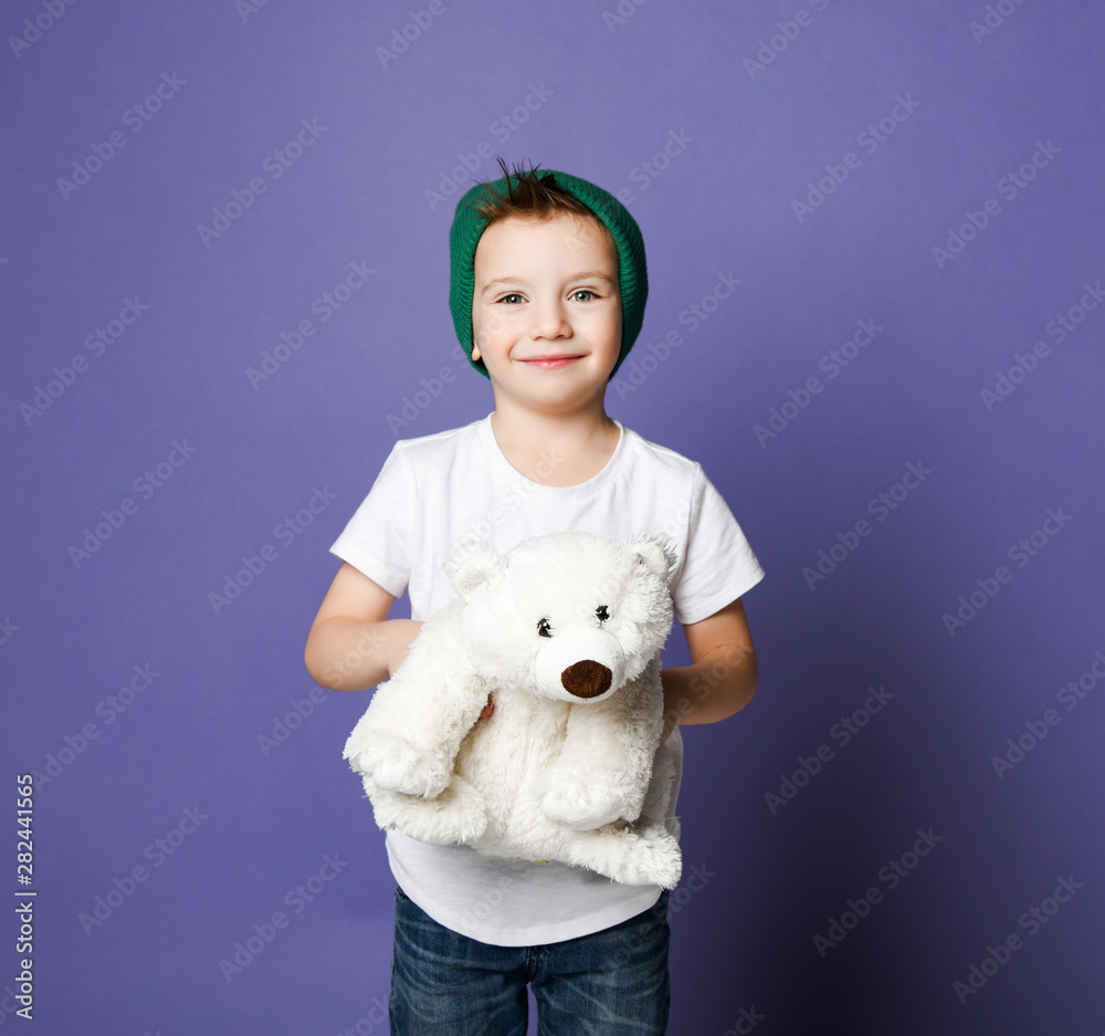 Portrait of kid boy in green hat showing us his favorite toy polar bear on purple. International day of polar bear concept Portrait of kid boy in green hat showing us his favorite toy polar bear on purple. International day of polar bear concept