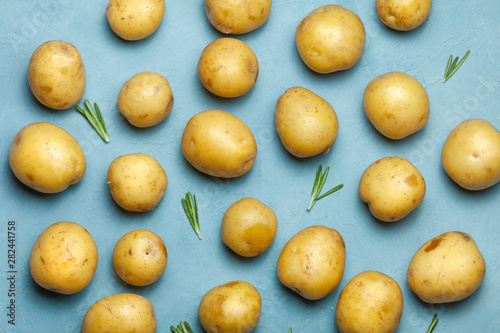 Raw potato tubers with rosemary on blue background