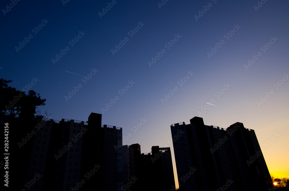 silhouette of buildings and airplane contrail