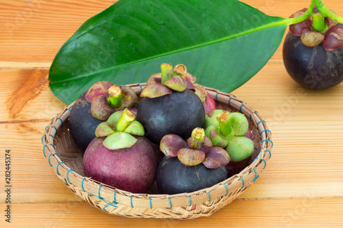Ripe mangosteens (Garcinia mangostana) with green leaves in a basket on the wooden table.