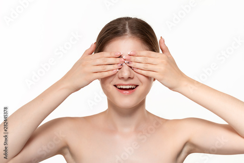 Close-up portrait of a beautiful young girl hiding behind her palms of hands isolated over white background.