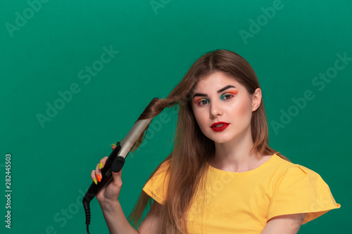 Portrait of beautiful young woman with bright color make-up having probems doing hair style herself with a curling iron.