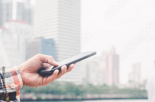 close up handsome man using hand typing mobile phones and touch screen working search with app devices outdoor in city with sunrise and building background. 5G technology connecting the world.
