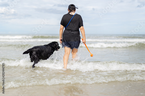 Woman playing ball with dog on the beach.