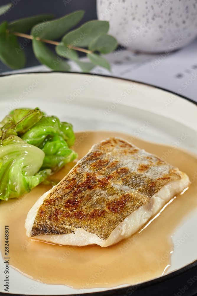 Delicious fish cooked in an oven and garnished with sauce and cabbage.