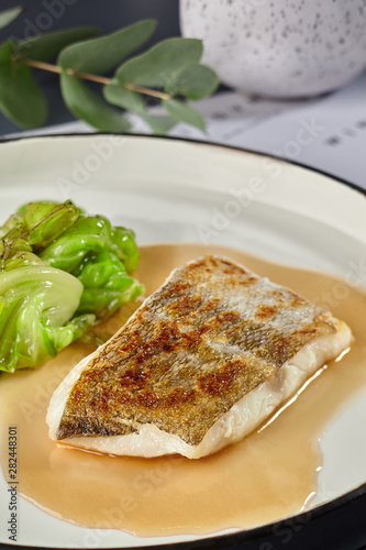 Delicious fish cooked in an oven and garnished with sauce and cabbage.