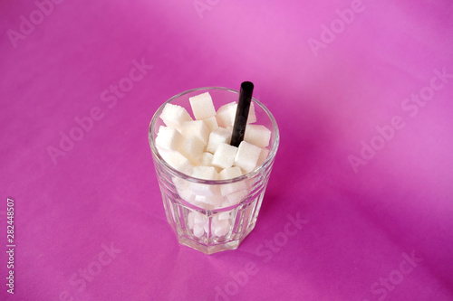 Glass full of sugar cubes  on purple background. Diabetes, sugar disease, unhealthy food, diet concept. Copy space