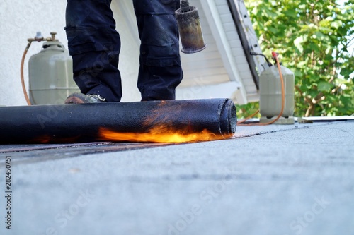 Flat roof installation with propane blowtorch during construction works with roofing felt. Heating and melting bitumen roofing felt. Roofing felt. Roofer working. Roofer working tool. Waterproofing photo