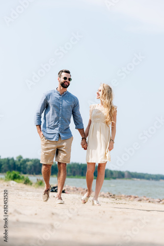 adult happy couple walking along beach and holding hands
