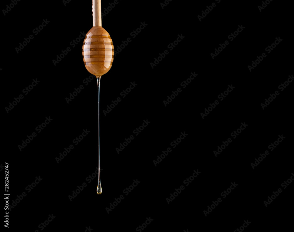 Honey flows from a stick on a black background. A drop of honey on a stick on a black background. Honey flows from a stick on a black background. A drop of honey on a stick on a black background.