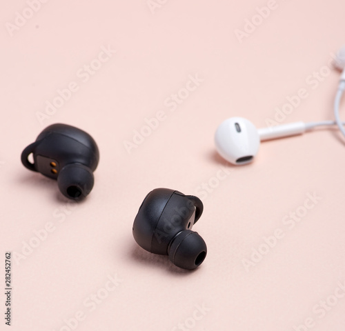 black wireless and white earphones with wire on a beige background