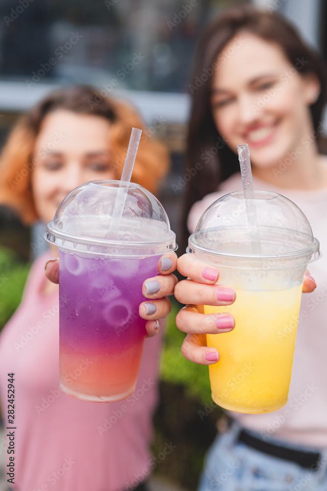 08.12.2018 Vinnitsa, Ukraine: two girlfriends hold in hands extended 2 multicolored cocktails with ice, girlfriends faces blurred 08.12.2018 Vinnitsa, Ukraine: two girlfriends hold in hands extended 2 multicolored cocktails with ice, girlfriends faces blurred