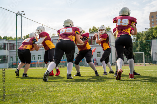 Full-length photo of sportive women playing american football on green lawn