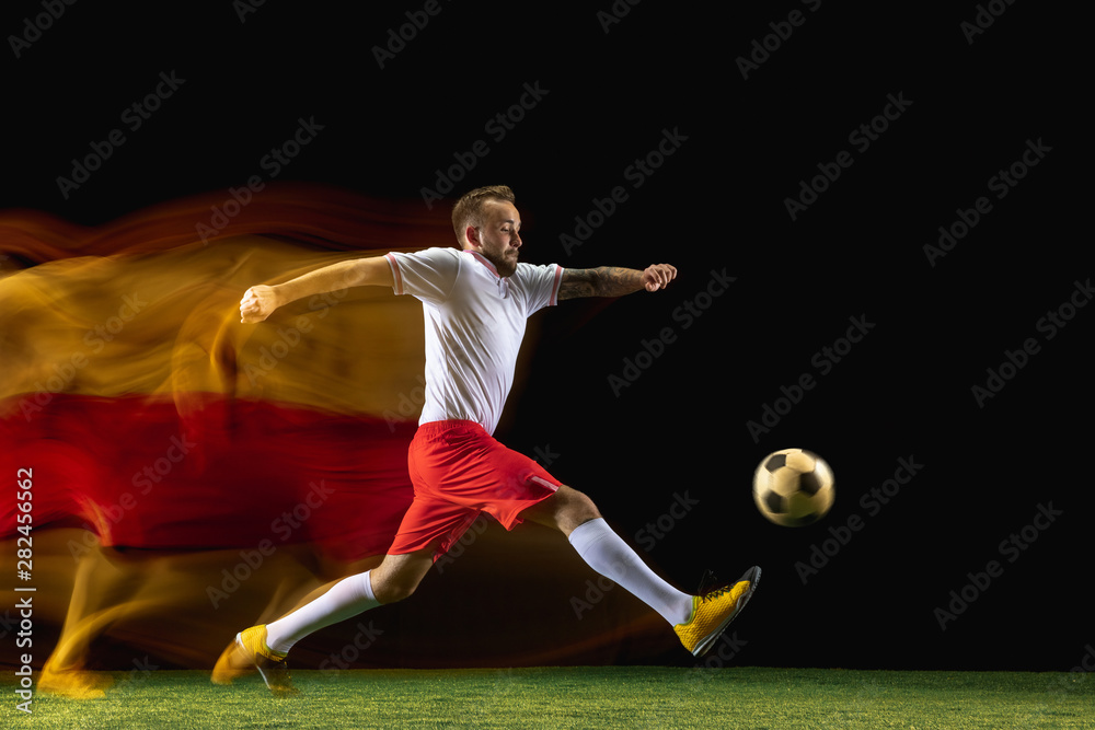 First. Young caucasian male football or soccer player in sportwear and boots kicking ball for the goal in mixed light on dark background. Concept of healthy lifestyle, professional sport, hobby. First. Young caucasian male football or soccer player in sportwear and boots kicking ball for the goal in mixed light on dark background. Concept of healthy lifestyle, professional sport, hobby.