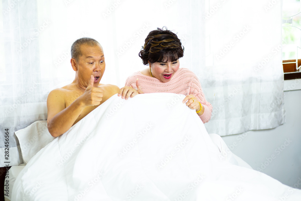 Elderly couples Feeling good looking down at his underwear at his penis under white covers sheet in badroom