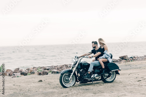 young couple of bikers on black motorcycle at beach near river