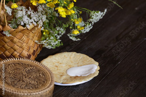 National traditional food for the holiday. Pancakes with sour cream. Wicker basket with flowers stands on a wooden table.
