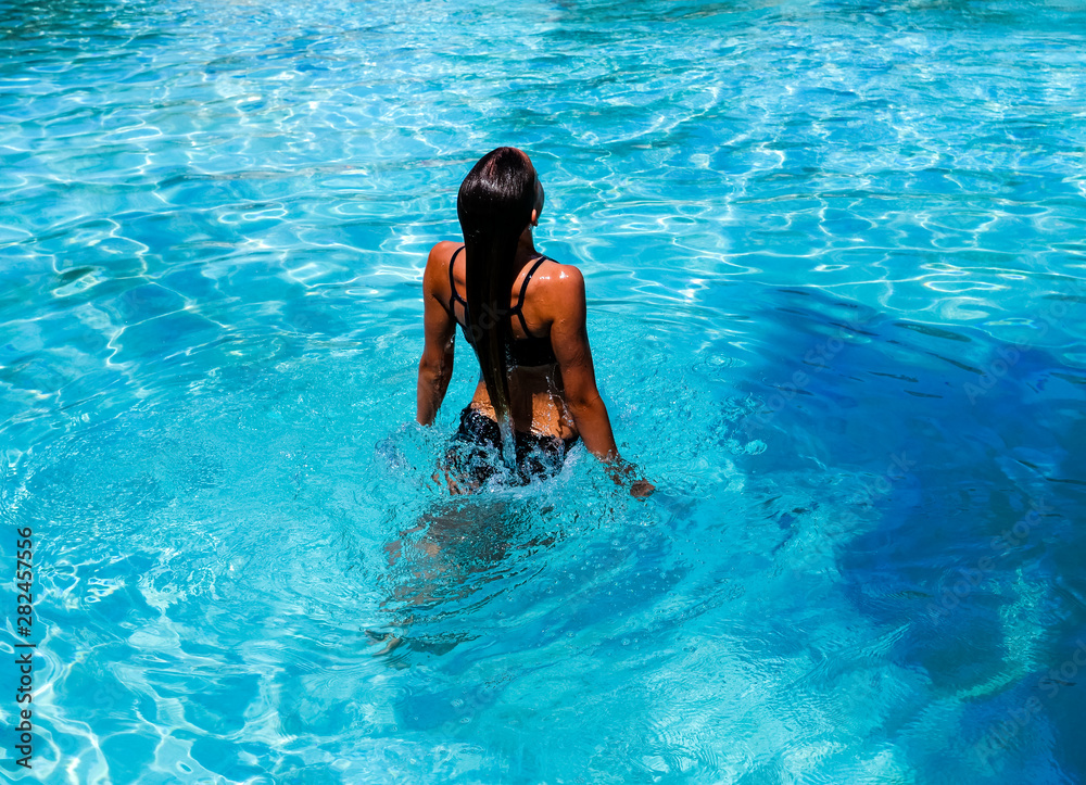 Pretty athletic sun tanned girl splashing in a swimming pool on vacation