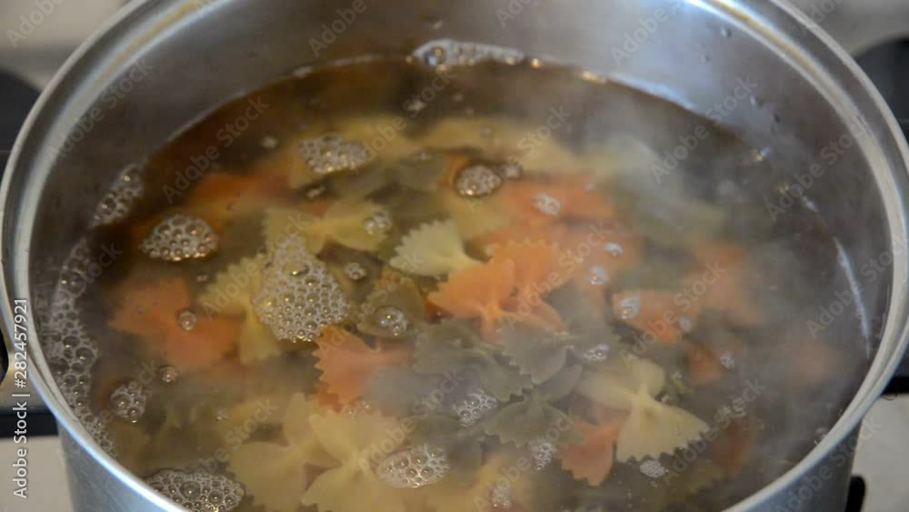 caucasian woman puts colorful bow pasta farfalle in boiling water in metal bowl, close up top view of full hd stock video footage caucasian woman puts colorful bow pasta farfalle in boiling water in metal bowl, close up top view of full hd stock video footage