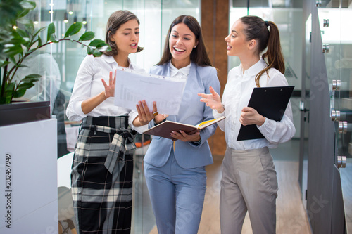 Three beautiful young business woman discussing documents in office lobby