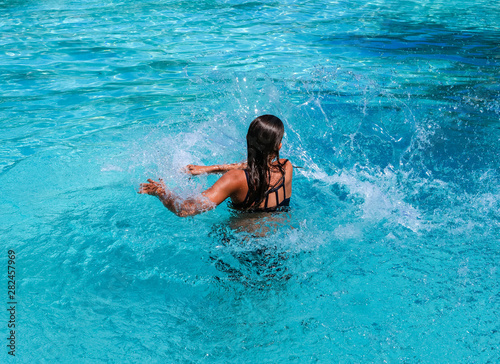 Pretty athletic sun tanned girl splashing in a swimming pool on vacation