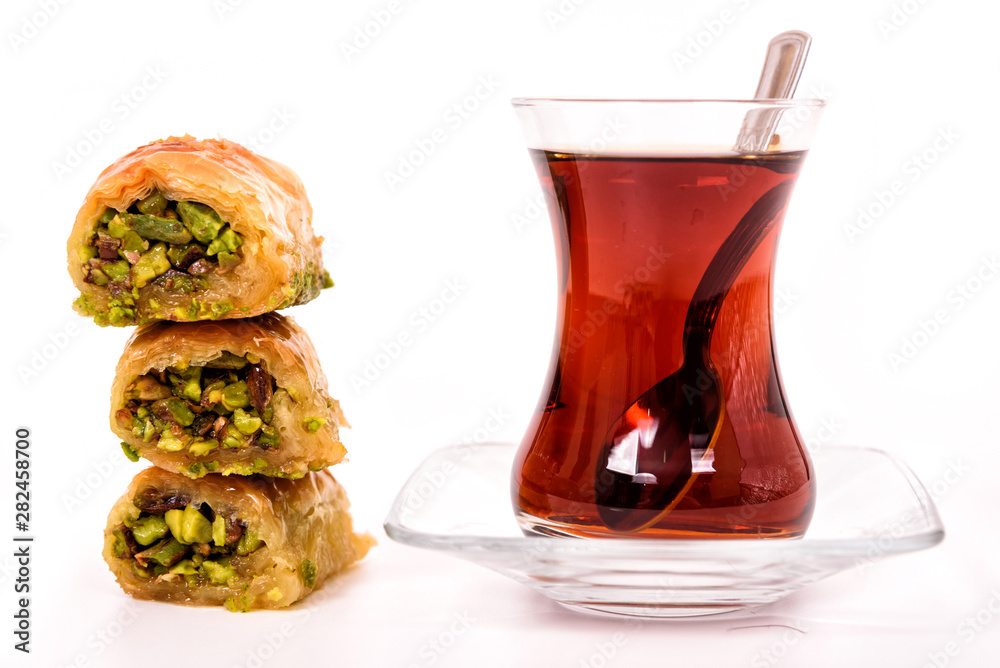 Traditional Turkish Dessert, Baklava on the wooden plate with pistachio nuts and Turkish Tea with spoon on the white surface. Traditional Turkish Dessert, Baklava on the wooden plate with pistachio nuts and Turkish Tea with spoon on the white surface.