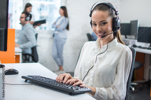 Friendly young woman working in call center office with team as the customer care operators