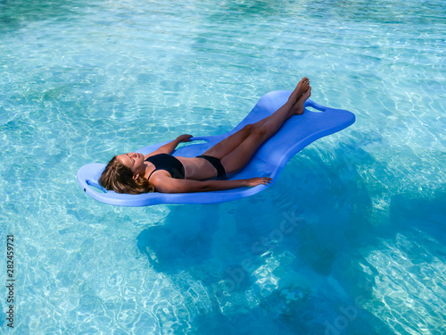 Pretty athletic sun tanned girl floating on a pool float in a swimming pool on vacation