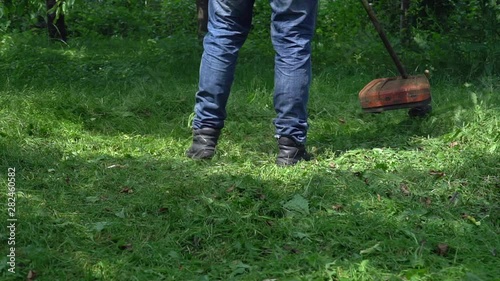 Close up. Man Gardener mowing lawn  with gasoline brush cutter, slow motion. Lawn mowing.