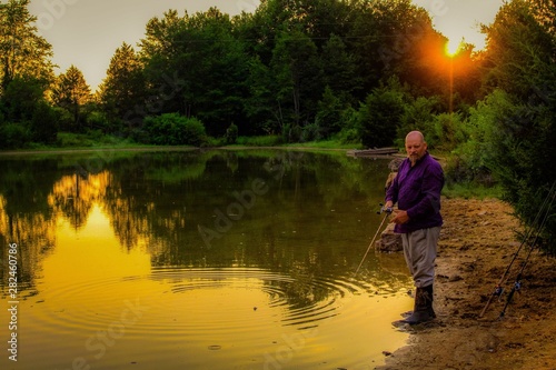 Peaceful Scene of Middle Aged Man Fishing on a Country Pond at Sunset with Golden filtered light reflected on pond