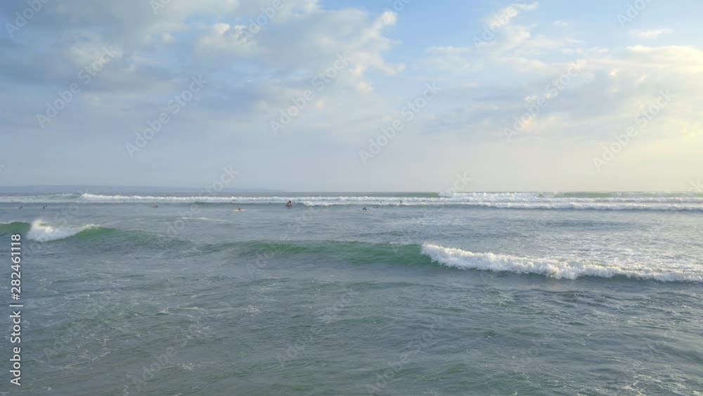 Tropical beach with big foamy waves and surfers swimming in water during sunset Tropical beach with big foamy waves and surfers swimming in water during sunset
